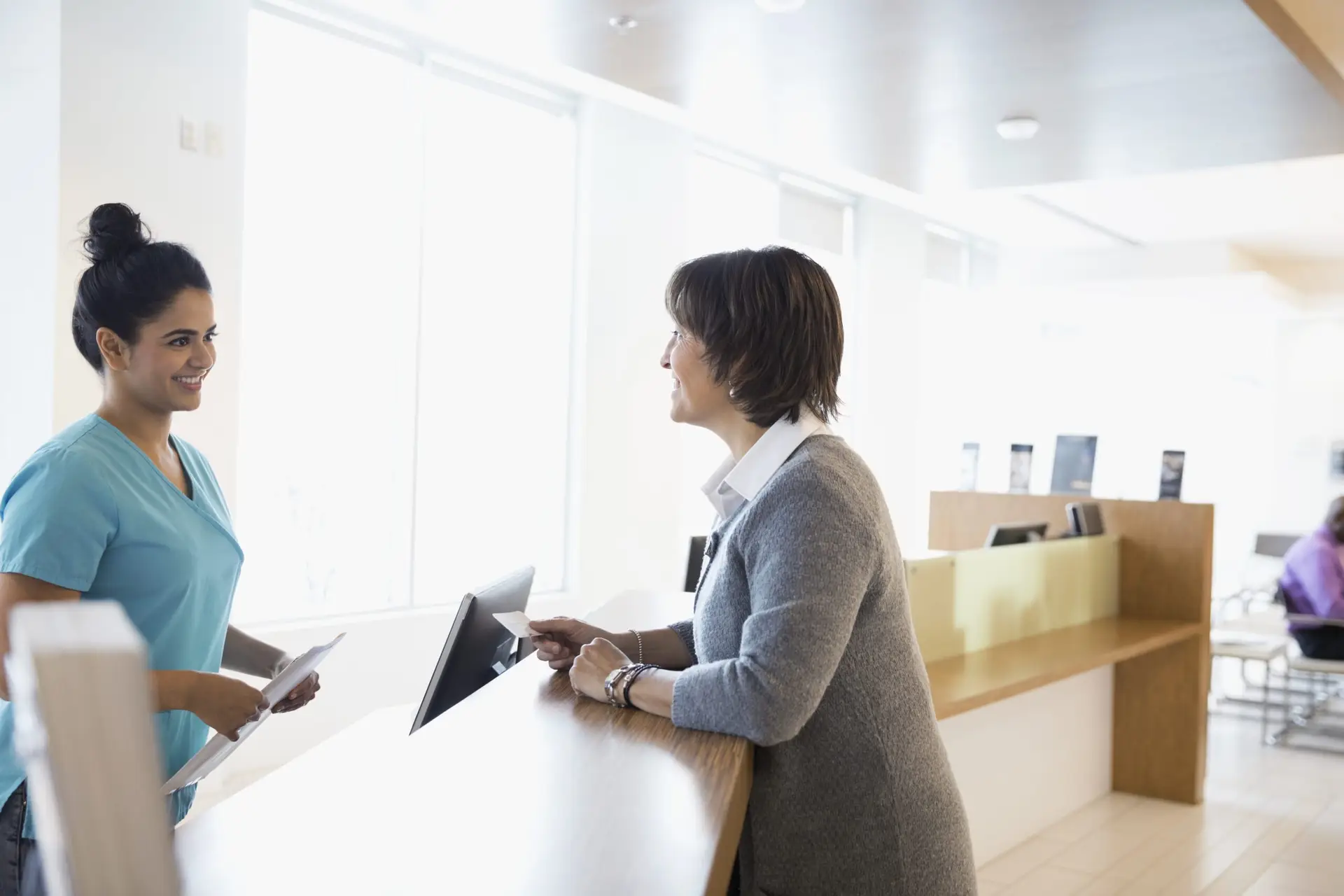 Female patient paying insurance copayment to nurse with credit card at clinic check-in counter